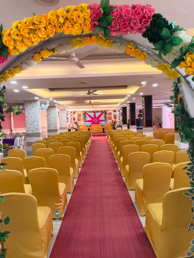 Floral archway framing rows of gold chairs and a red carpet aisle inside the Jagan Palace hall